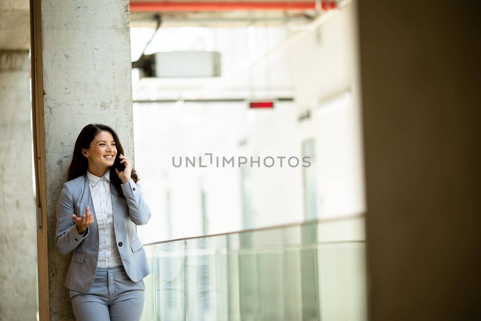 Pretty young business woman using mobile phone in the office hallway
