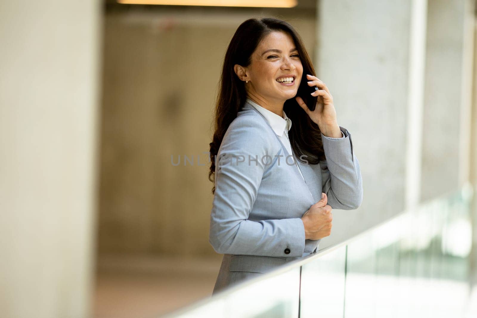 Pretty young business woman using mobile phone in the office hallway