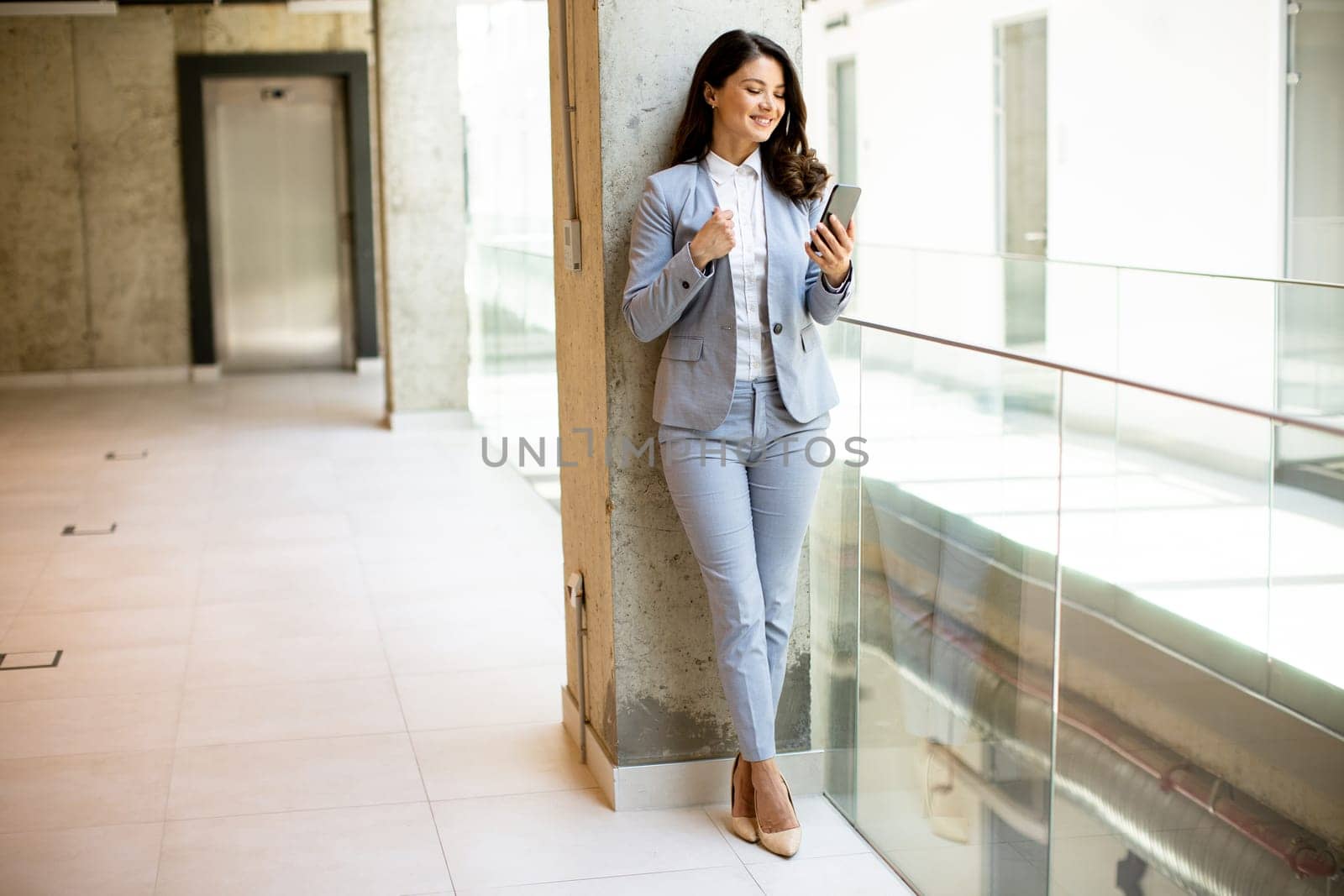 Pretty young business woman using mobile phone in the office hallway