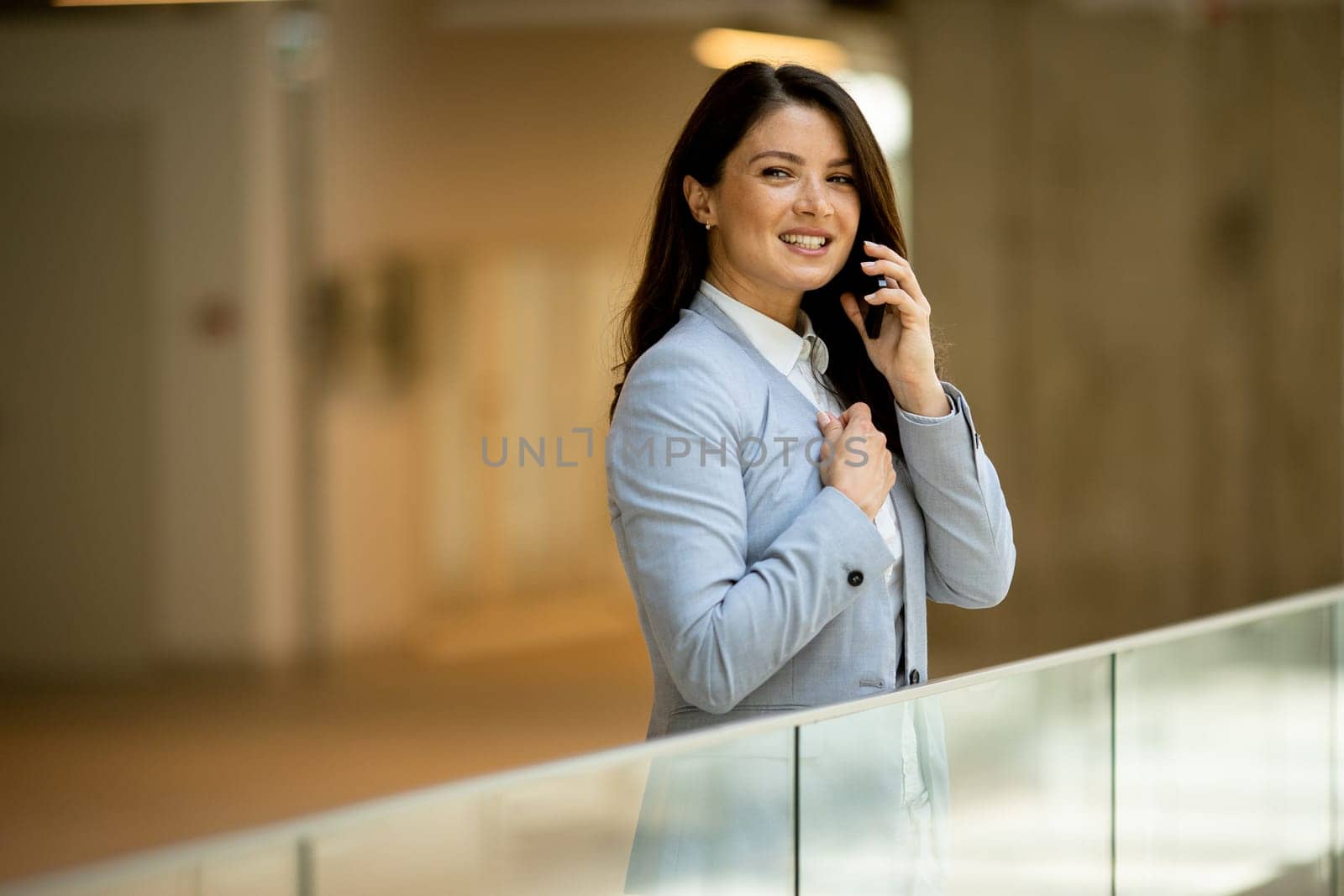 Pretty young business woman using mobile phone in the office hallway