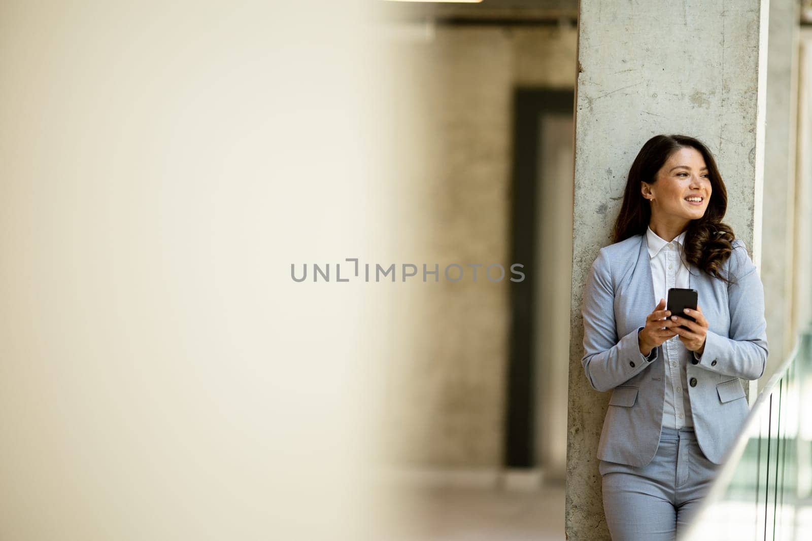 Pretty young business woman using mobile phone in the office hallway