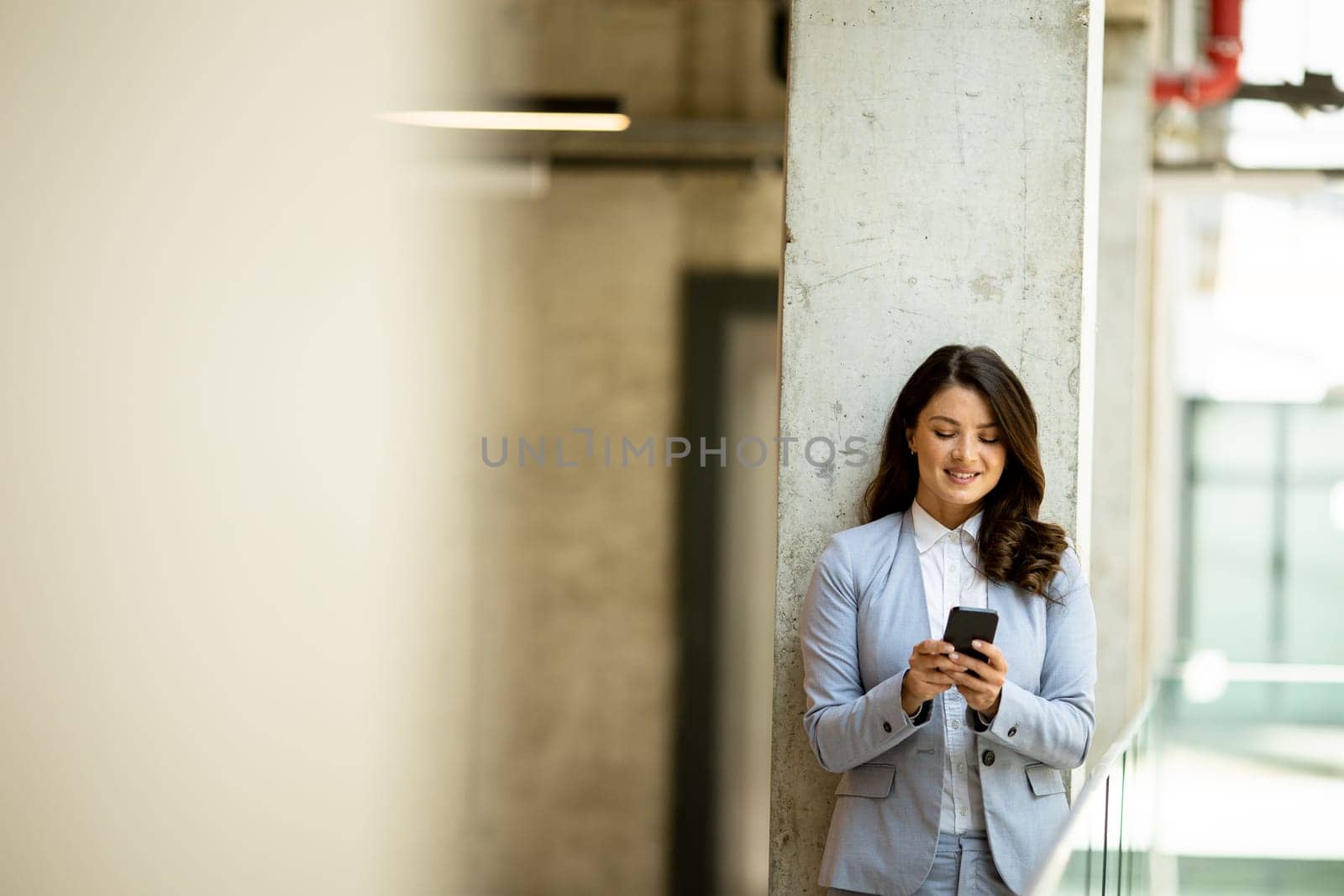 Pretty young business woman using mobile phone in the office hallway