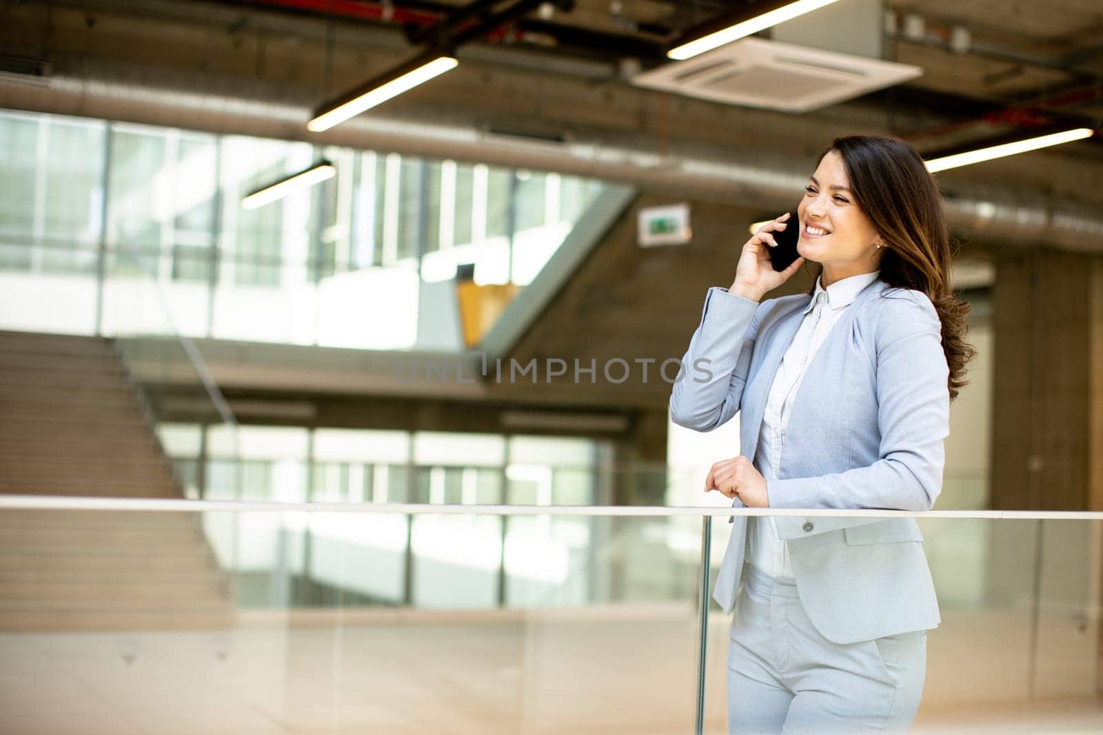 Pretty young business woman using mobile phone in the office hallway