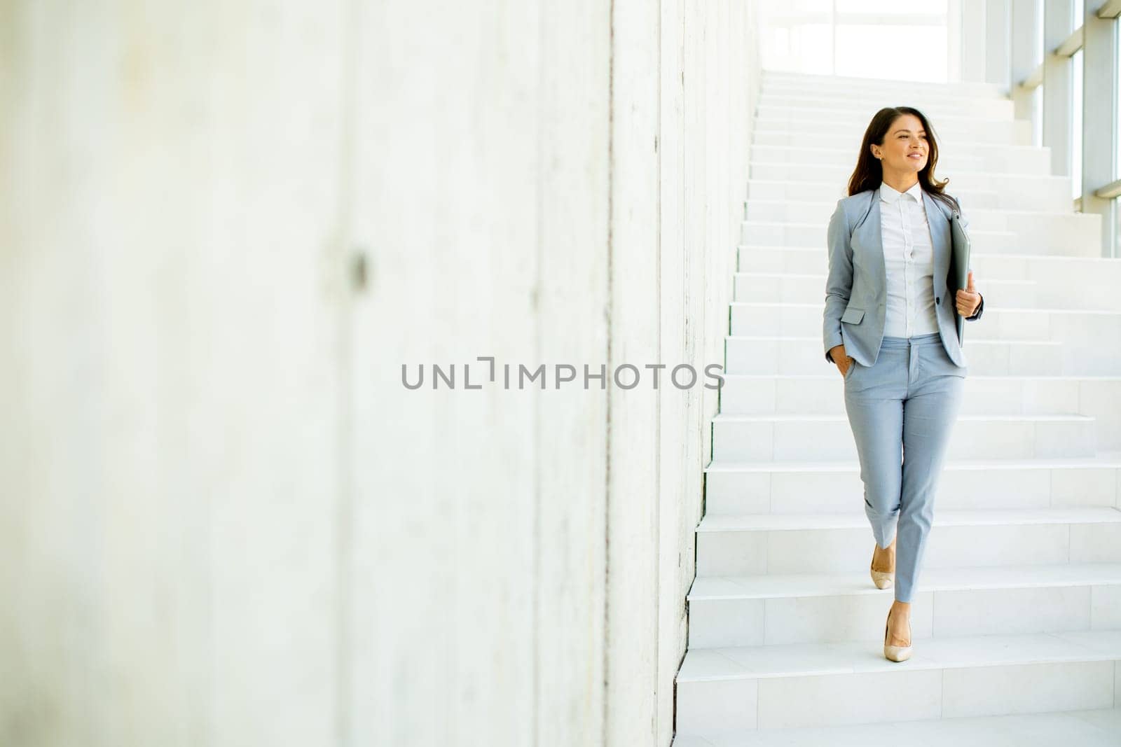 Young business woman walking down the stairs and holding laptop at the office hallway