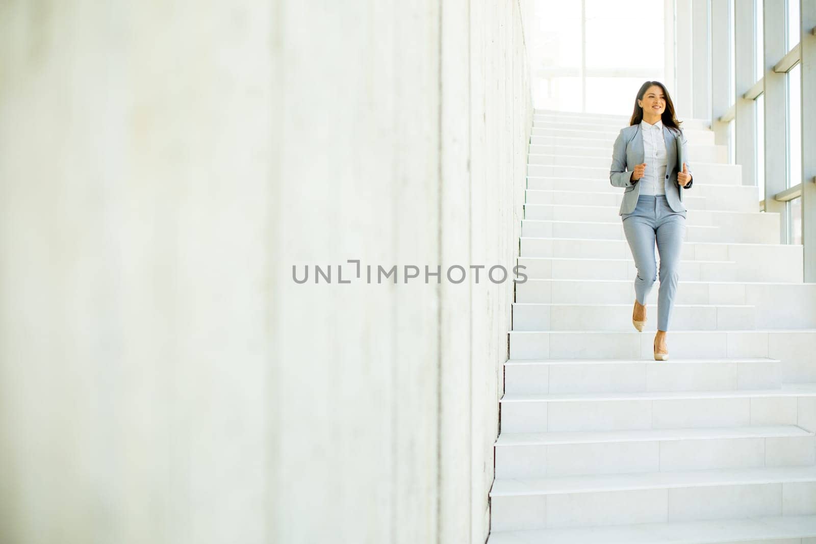 Young business woman walking down the stairs and holding laptop at the office hallway