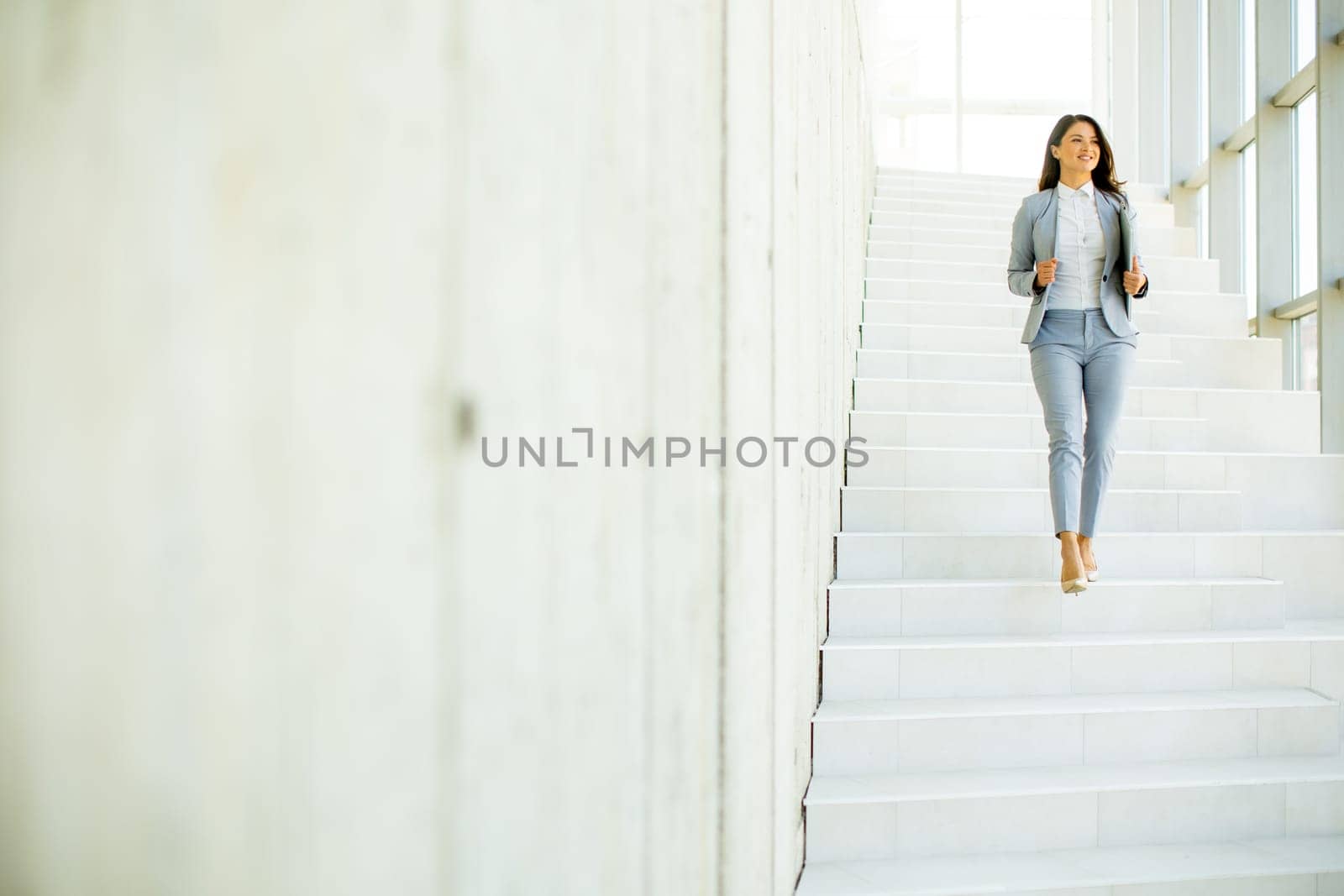 Young business woman walking down the stairs and holding laptop at the office hallway