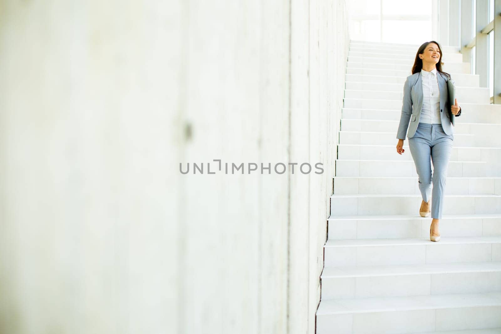 Young business woman walking down the stairs and holding laptop at the office hallway
