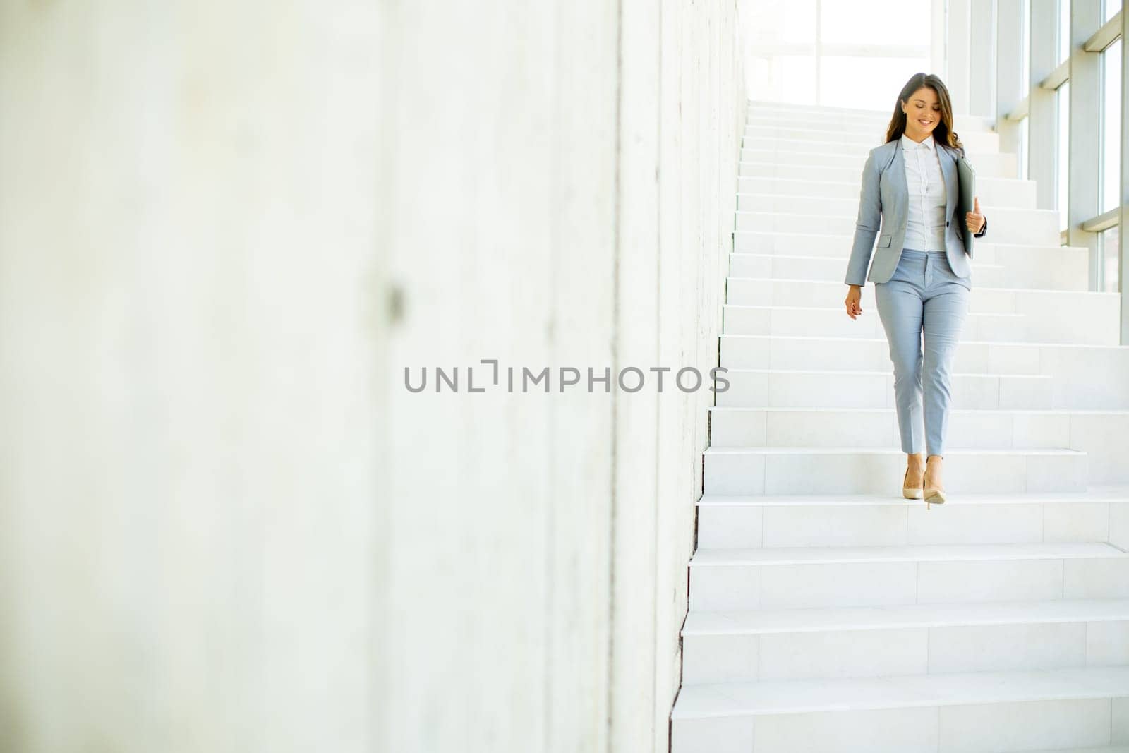 Young business woman walking down the stairs and holding laptop at the office hallway