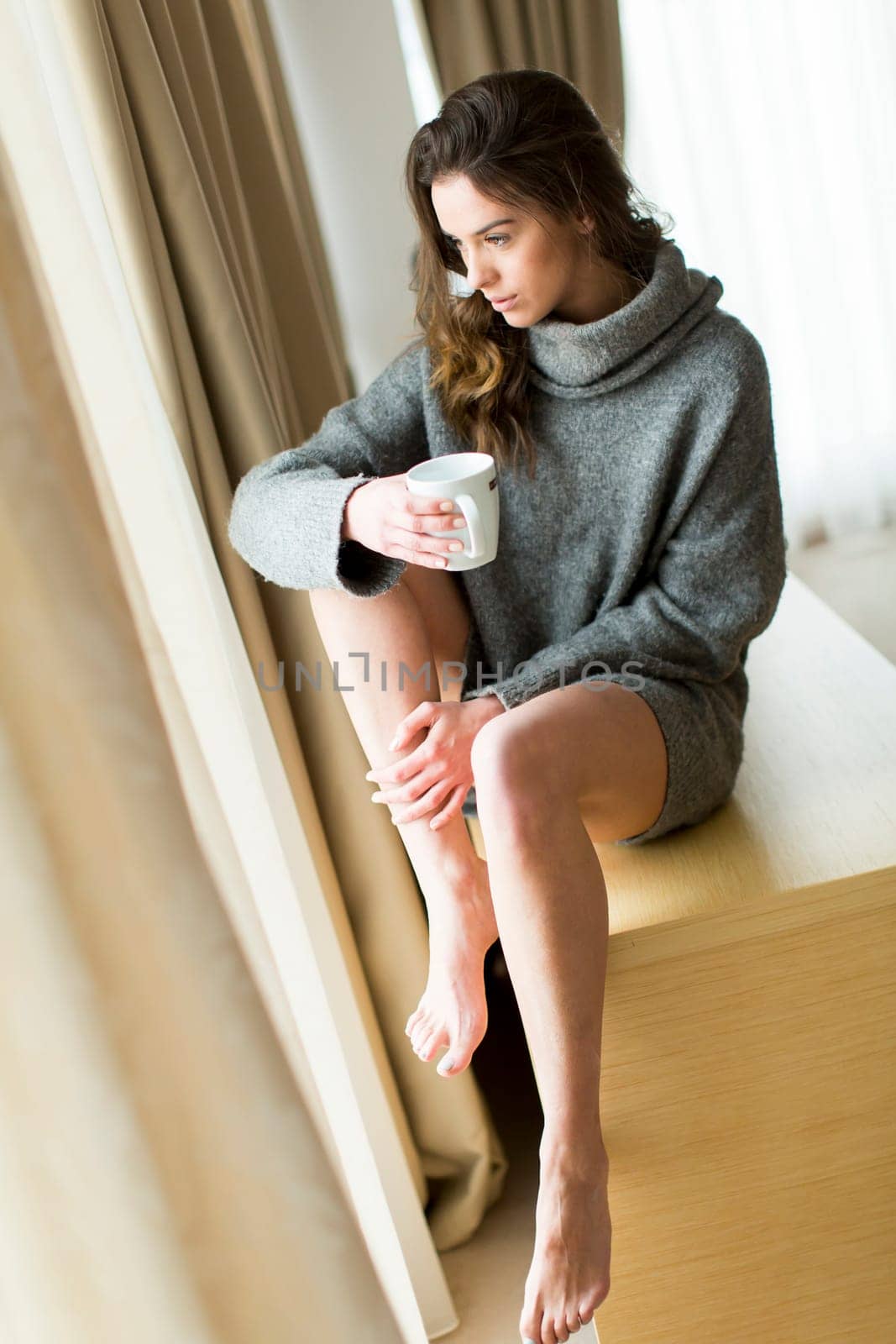 Pretty young woman with cup of coffee by the window