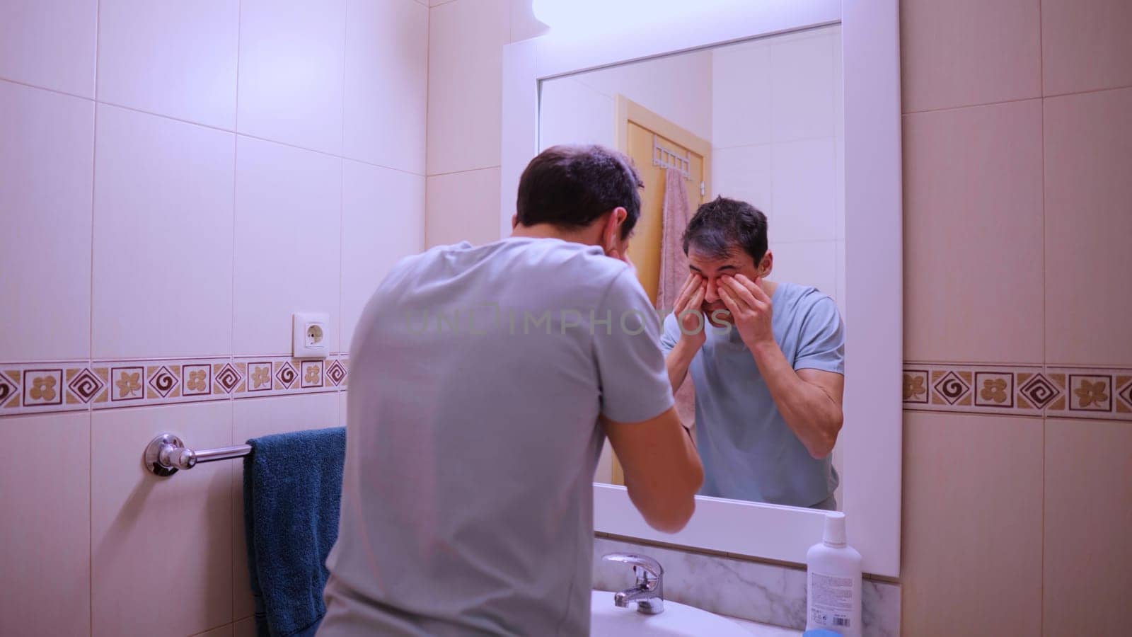 Man washes and dries his face looking at himself in the bathroom mirror