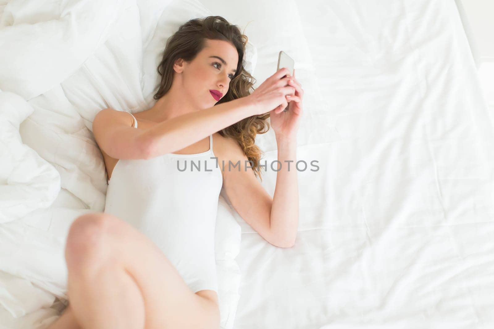 Young woman with smartphone in the bed