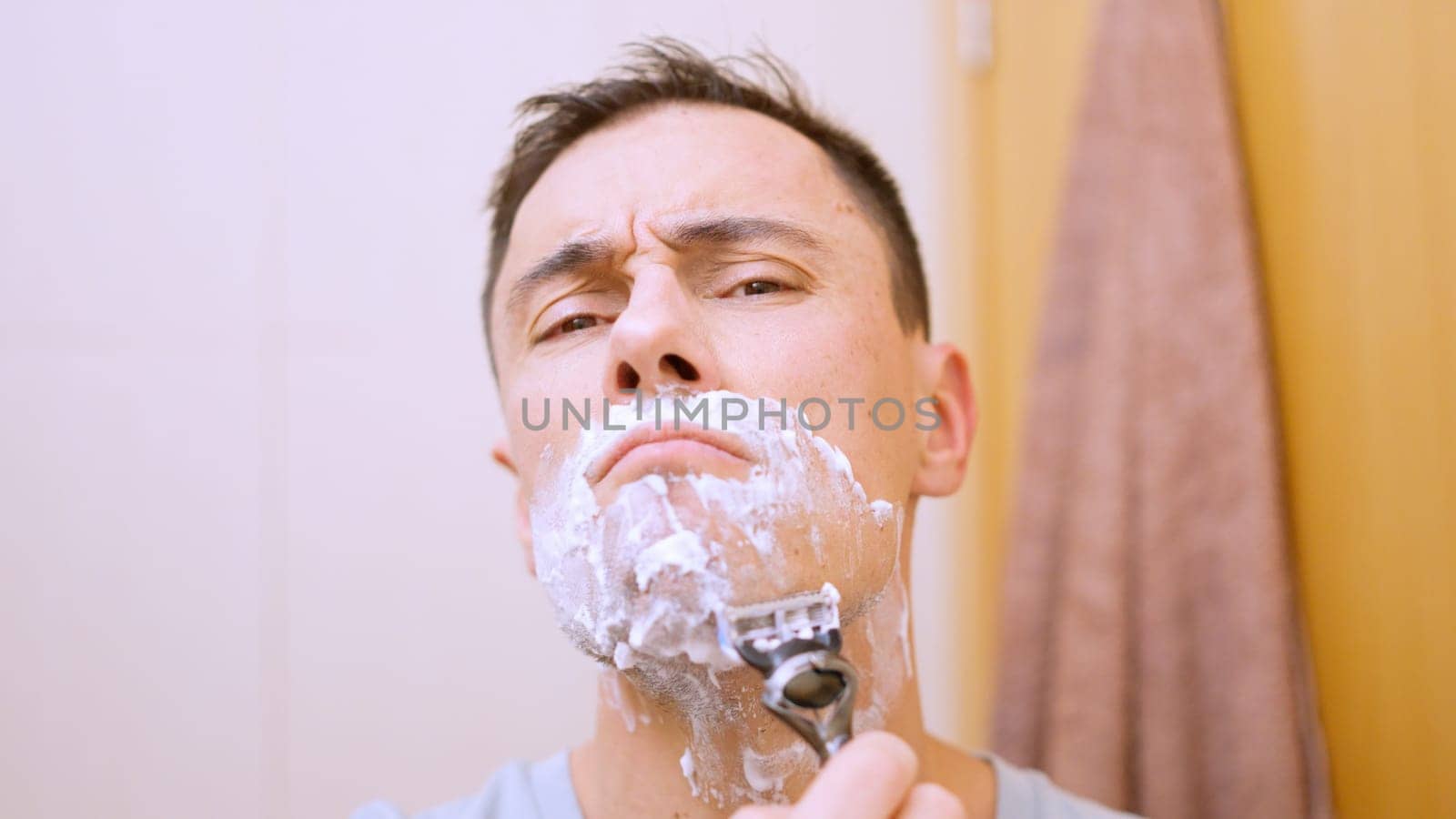 Caucasian man shaving his beard with a razor and shaving cream in the bathroom