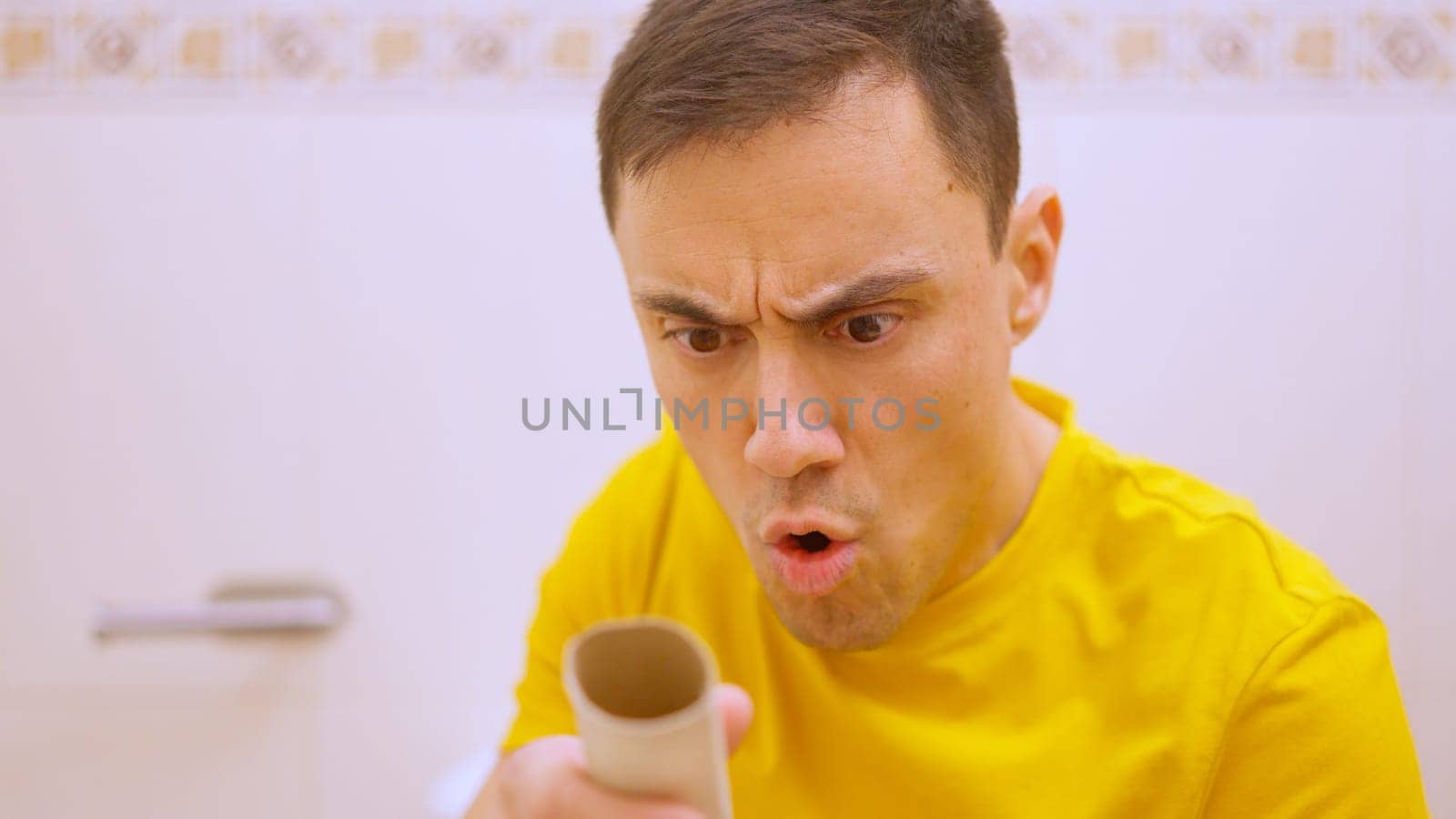 Man sitting on toilet discovers there is no toilet paper left on the roll and makes a surprised face