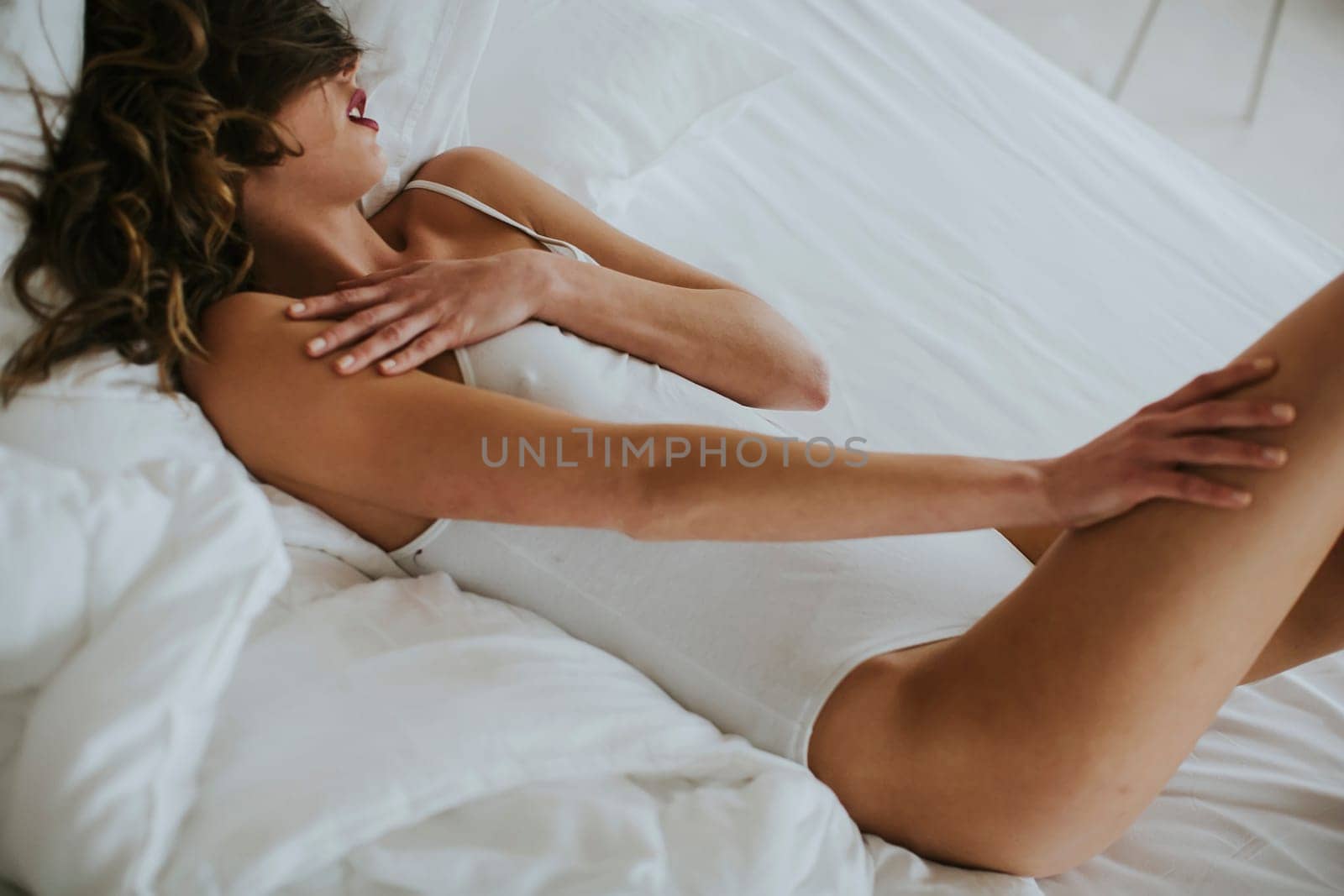 Attracttive young woman lies in white bed