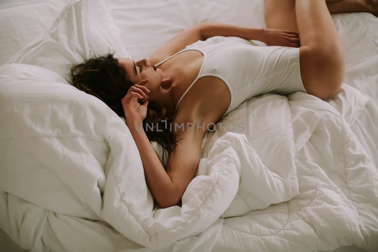 Attracttive young woman lies in white bed