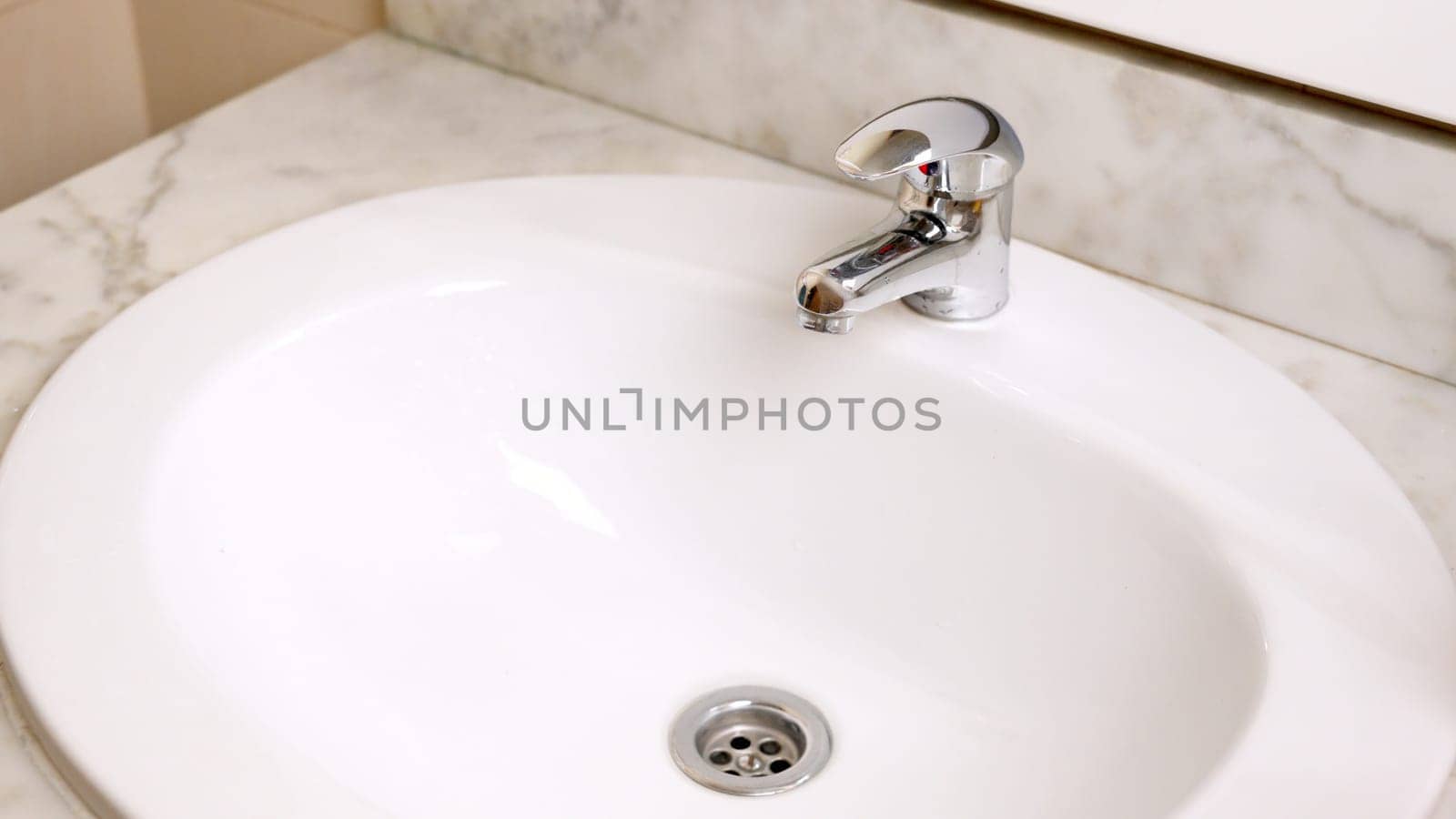 Clean white bathroom sink with chrome faucet on marble countertop