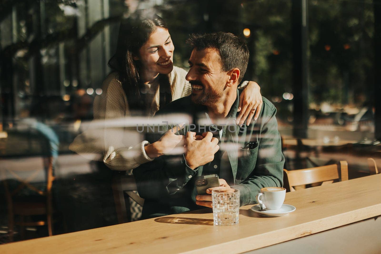 Young couple shares tender moments at a café, surrounded by greenery and natural light, as they connect over warm drinks and playful gestures
