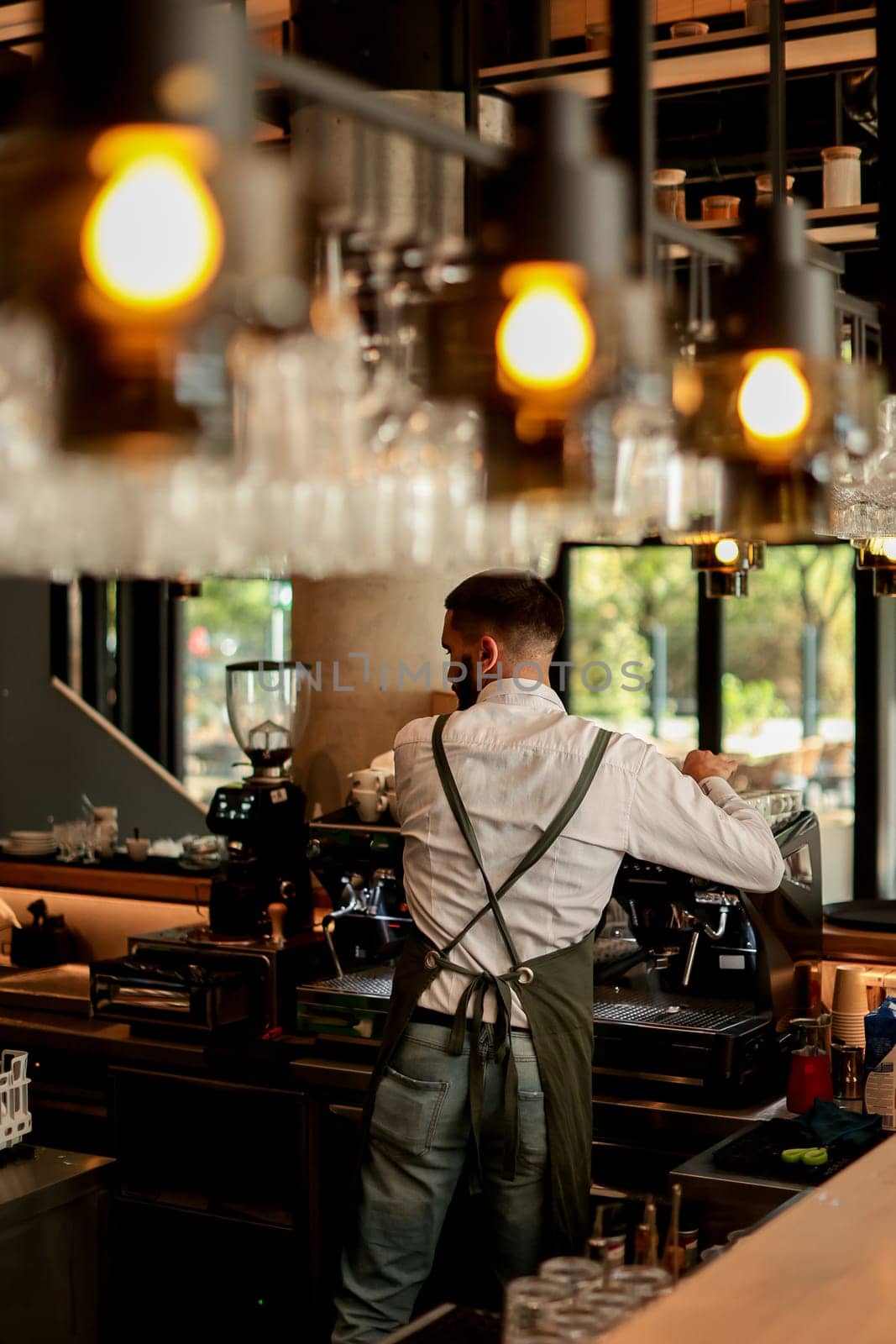 Dedicated barista expertly prepares espresso while engaging with a lively atmosphere filled with sunlight, plants, and happy customers savoring their drinks