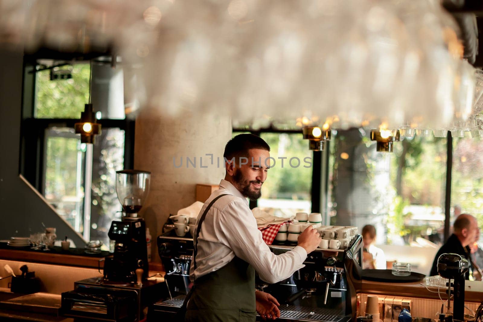Dedicated barista expertly prepares espresso while engaging with a lively atmosphere filled with sunlight, plants, and happy customers savoring their drinks