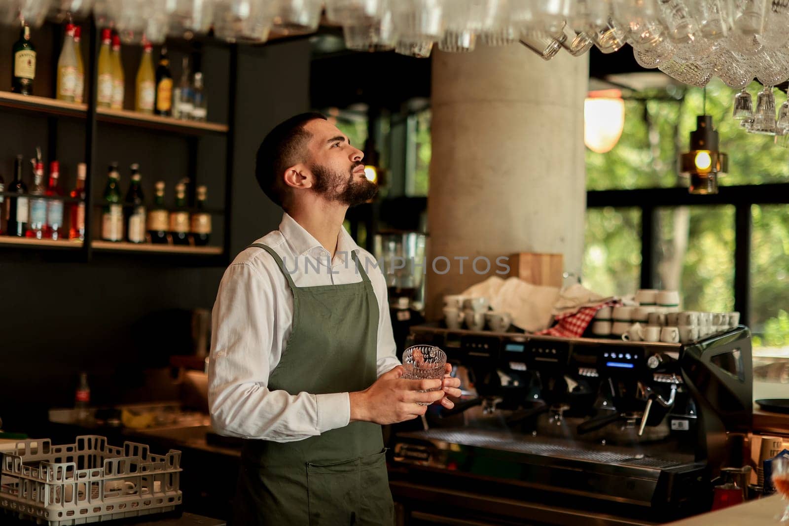Bartender in an elegant apron meticulously arranges glassware while serving patrons in a lively café environment, highlighting craft and hospitality