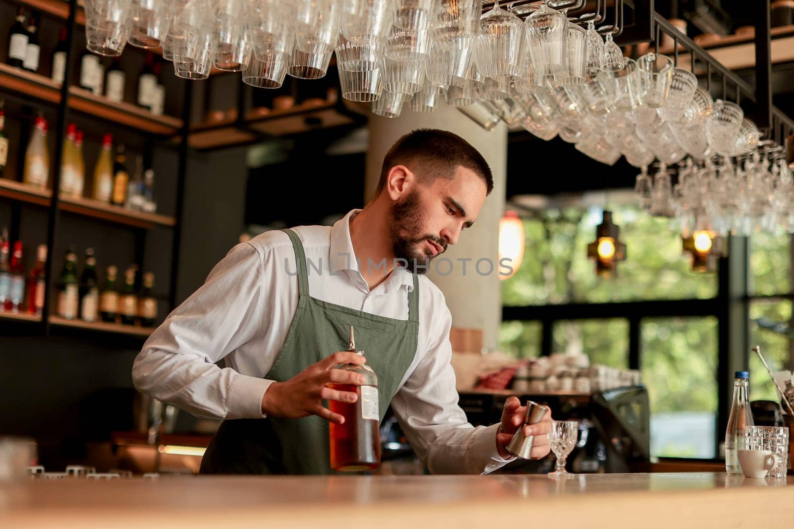 In a lively bar setting, a confident bartender mixes a fresh cocktail, showcasing his expertise with a bottle in hand, ready for the night's rush