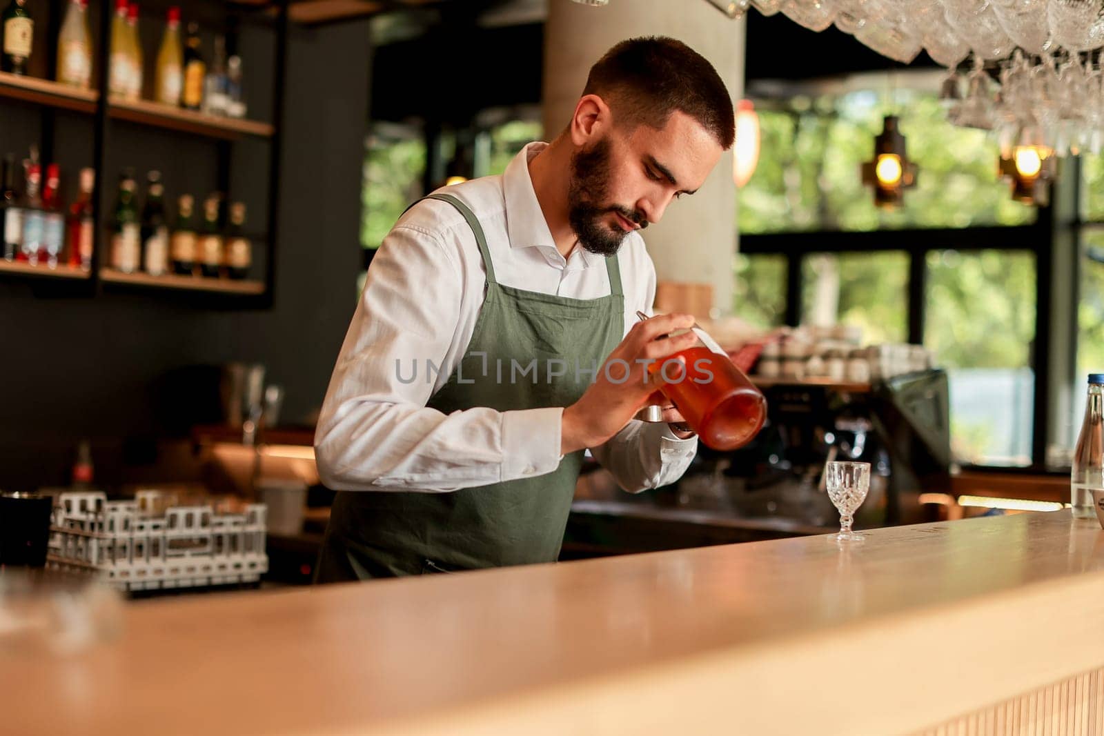 In a lively bar setting, a confident bartender mixes a fresh cocktail, showcasing his expertise with a bottle in hand, ready for the night's rush
