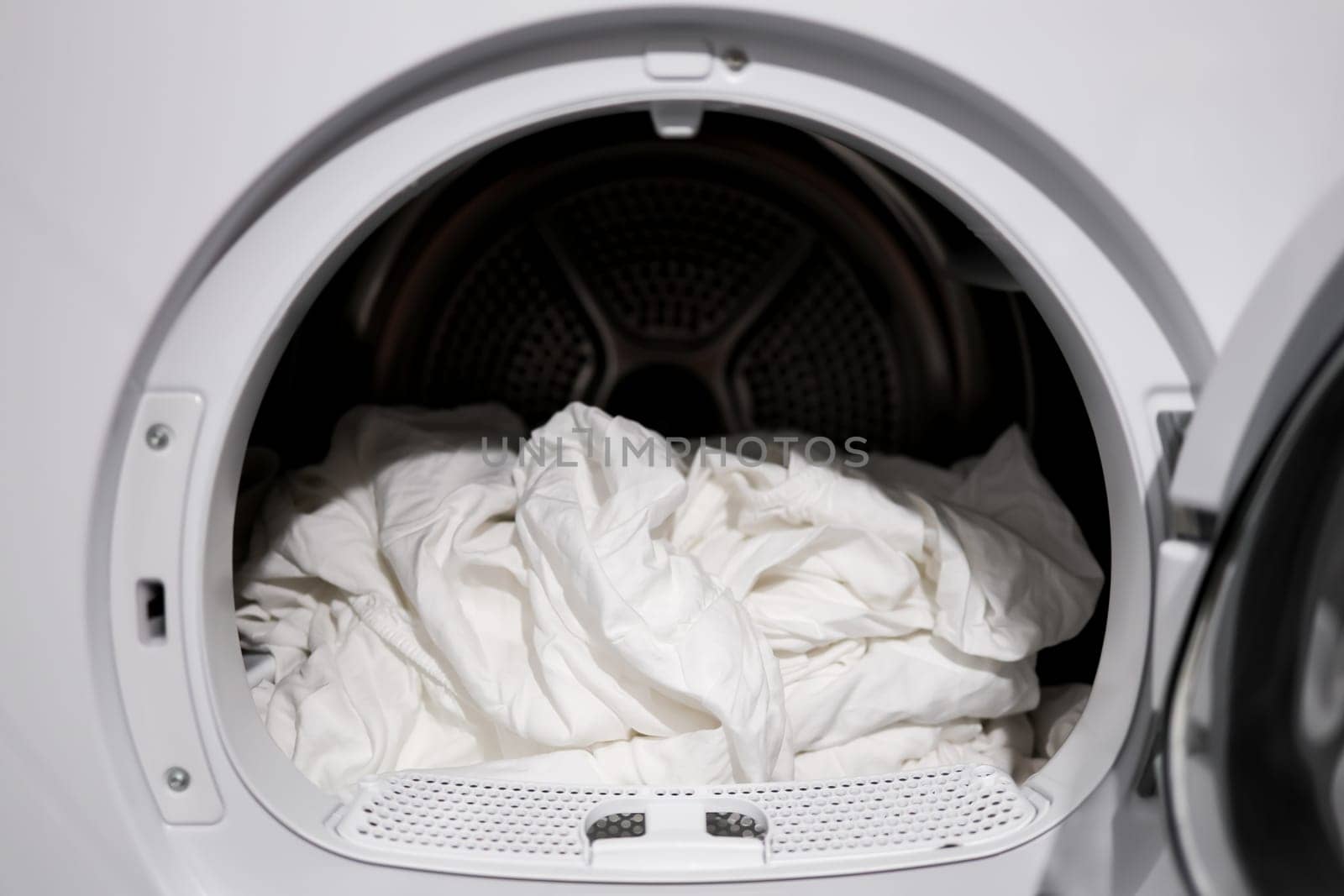 White bedsheets in modern tumble dryer close up laundry scene.