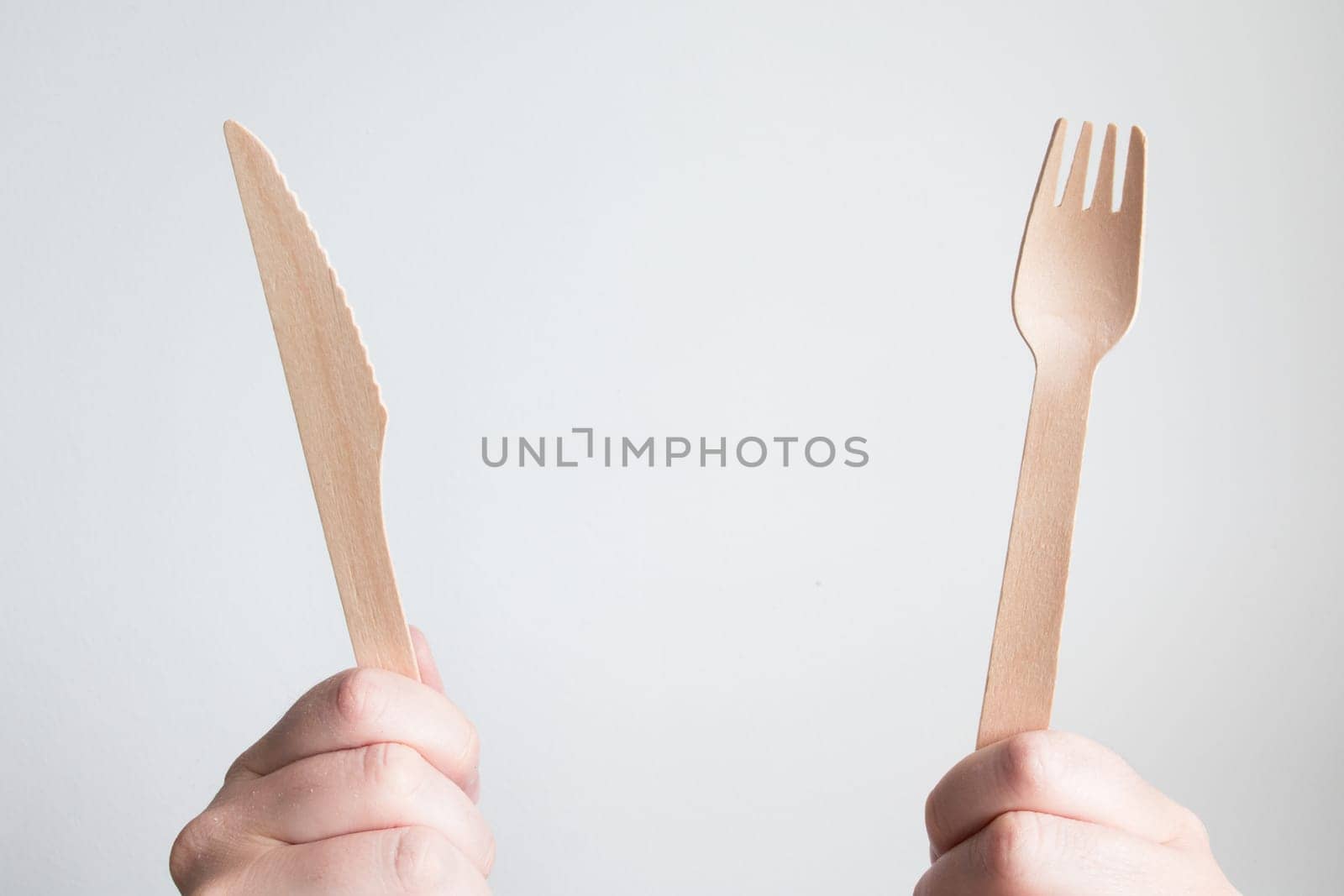 Hands holding wooden cutlery set against white background.