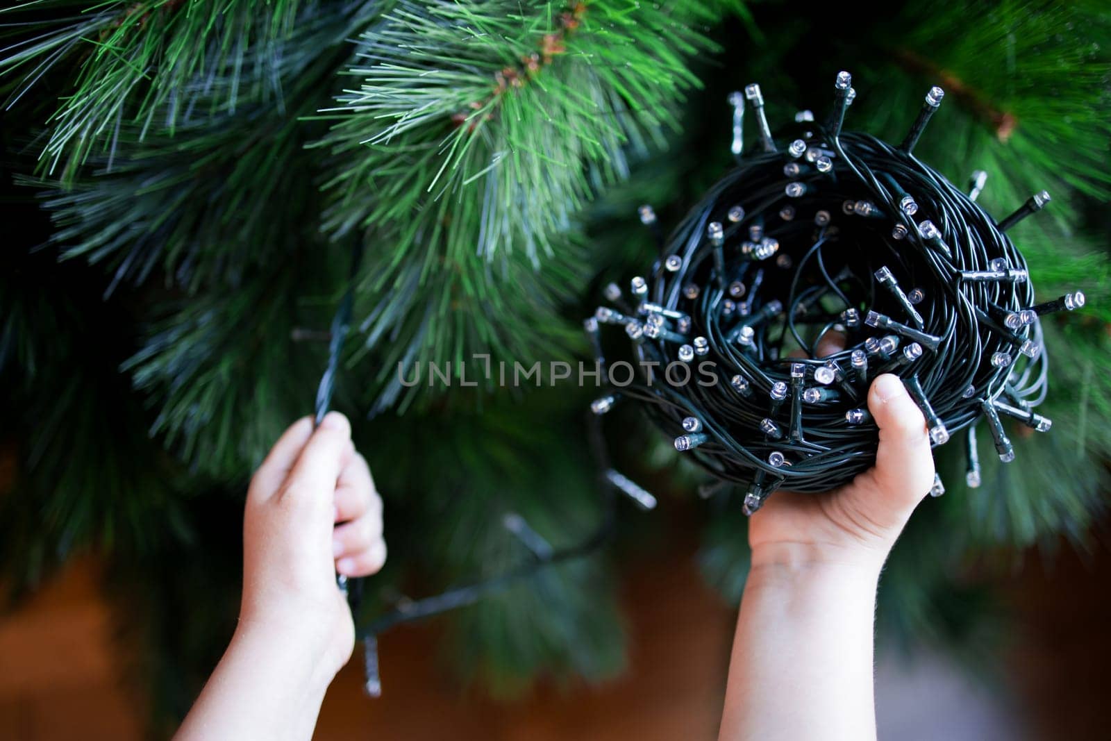 Child preparing Christmas tree with string lights.