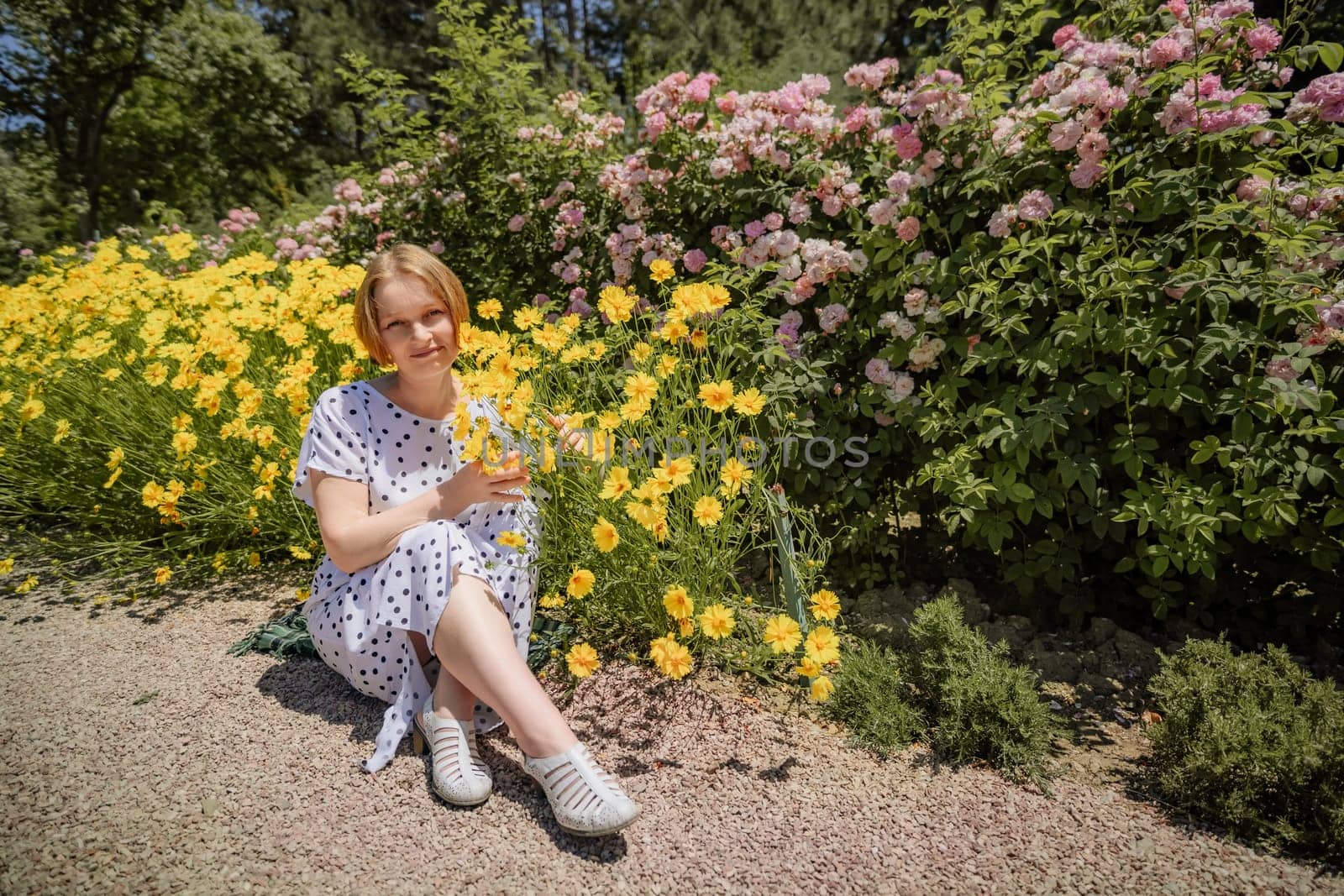 A woman is sitting in a field of yellow flowers. She is holding a glass of wine and smiling