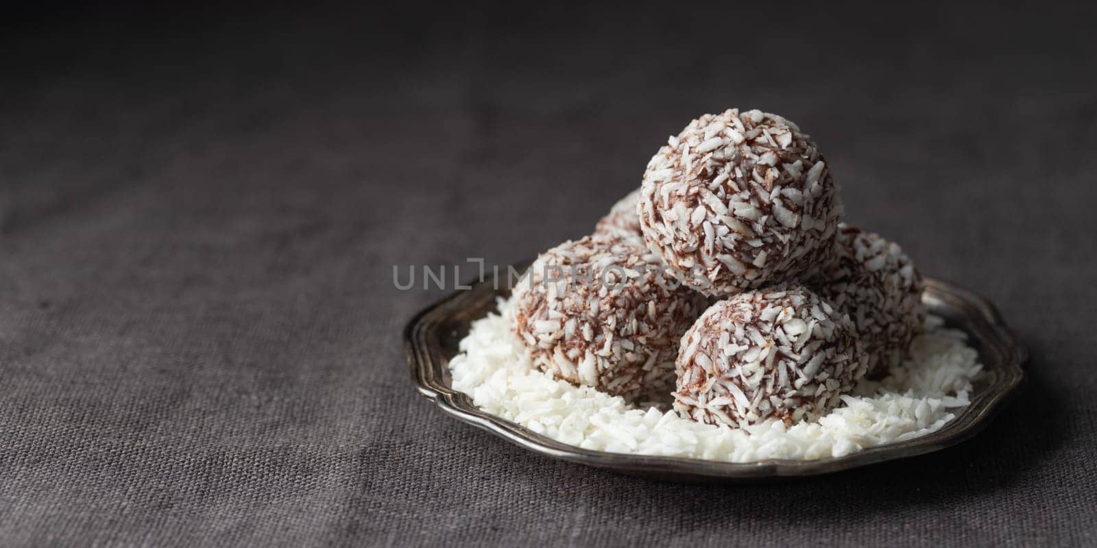 Artisan chocolate coconut truffle candies on dark background from confectionary. Handmade or handcrafted bonbons, chocolatier concept. Horizontal banner, copy space