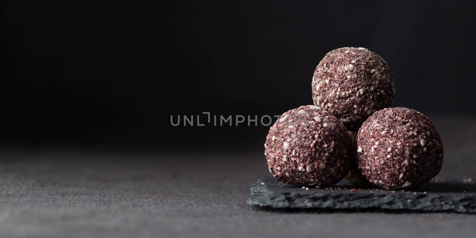 Artisan chocolate truffle candies with berry and fruit filling on dark marble background from confectionary. Handmade or handcrafted bonbons, chocolatier concept. Horizontal banner, copy space