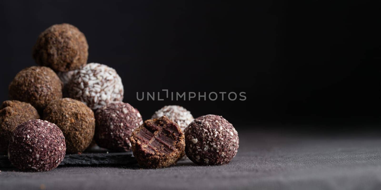 Assortment of gourmet handcrafted vegan chocolate truffle candies on dark background from premium confectionary. Bited handmade bonbon chocolatier concept. Horizontal banner with copy space
