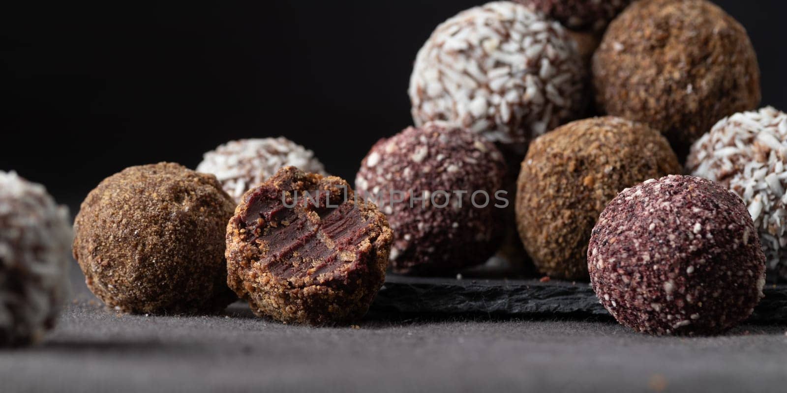 Assortment of gourmet handcrafted vegan chocolate truffle candies on dark background from premium confectionary. Bited handmade bonbon chocolatier concept. Horizontal banner with copy space