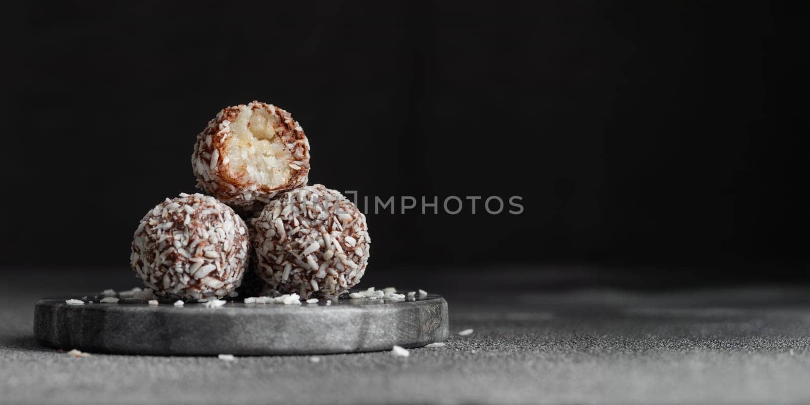 Artisan chocolate truffle candies with coconut filling on dark marble background from confectionary. Handmade or handcrafted bonbons, chocolatier concept. Horizontal banner, copy space