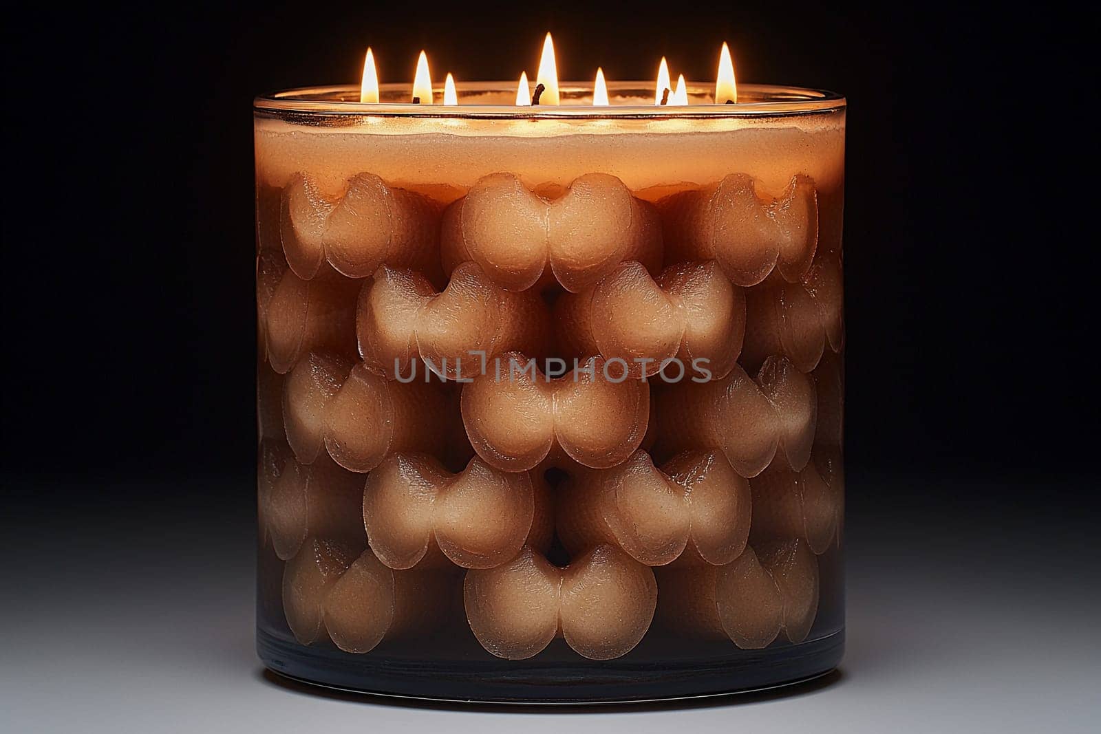 A candle with multiple wicks glows warmly against a dark backdrop, showcasing an eye-catching pattern of rounded shapes that enhances its aesthetic appeal.