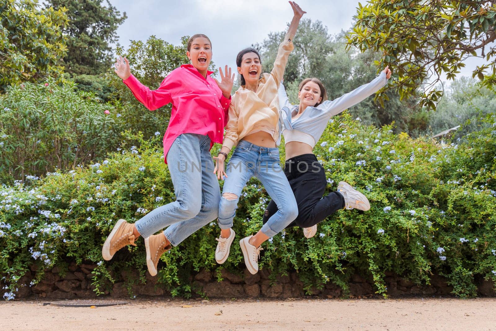 Happy young women jumping together in a lush green park, laughing and celebrating friendship. Dressed in casual outfits, they enjoy a fun and energetic moment in a vibrant outdoor setting.