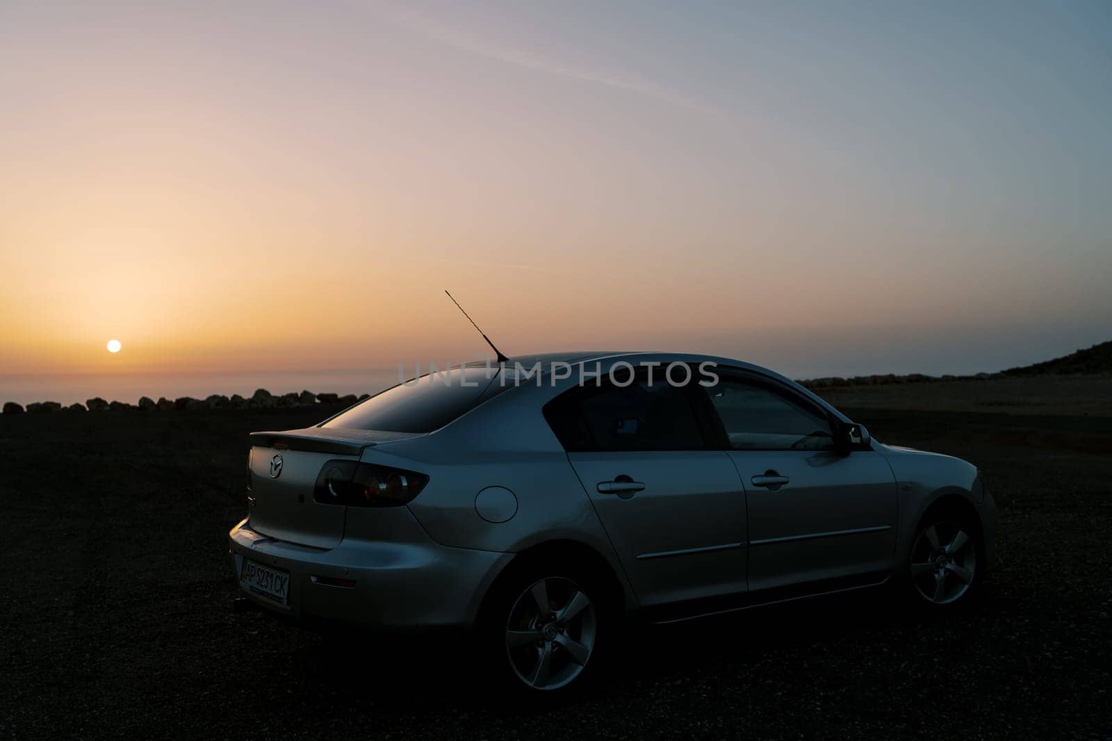 Silver car stands on the seashore against the backdrop of a colorful sunset. High quality photo
