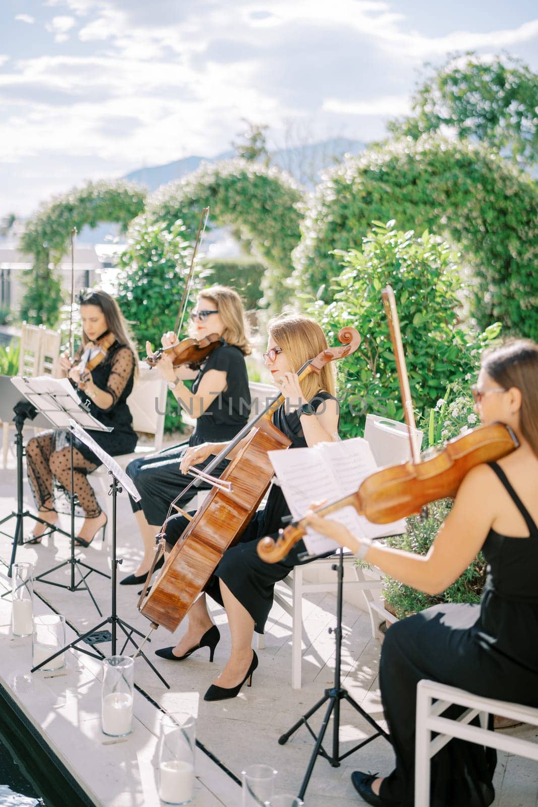Female string quartet plays violins and cellos while sitting on chairs in the garden. High quality photo