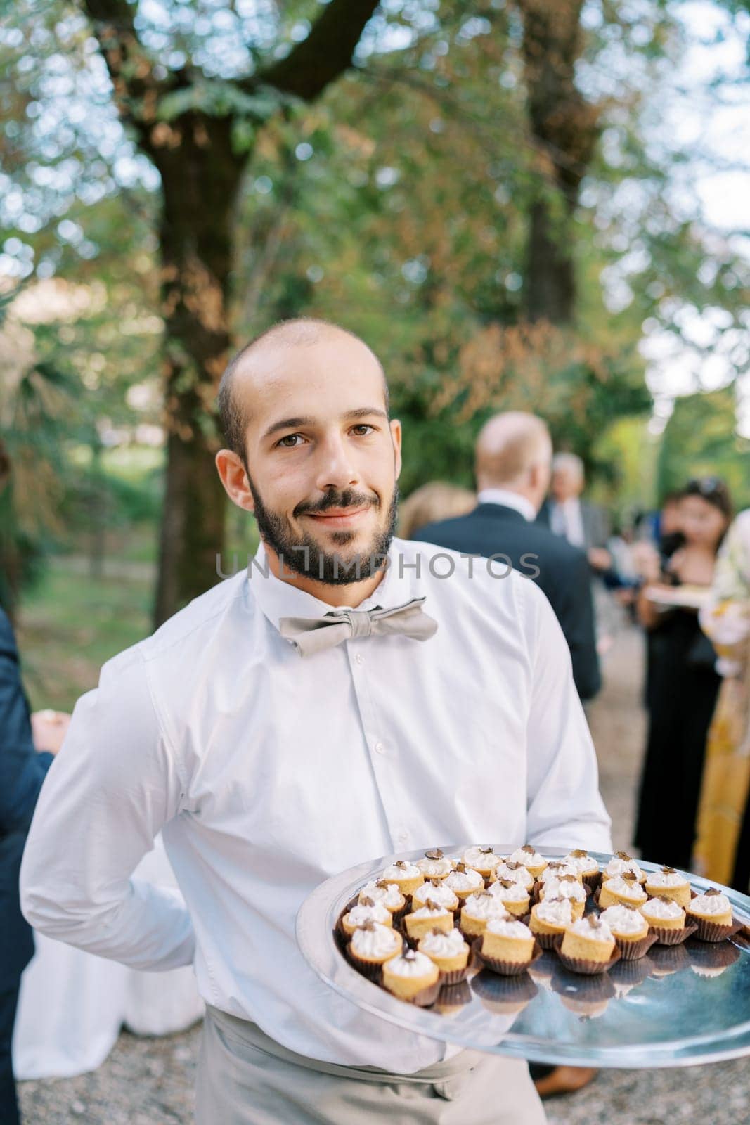 Smiling waiter with cupcakes on a tray standing in the park. High quality photo