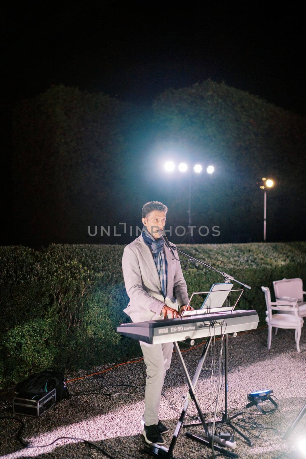 Band vocalist plays the synthesizer and sings in the night garden under the lights. High quality photo