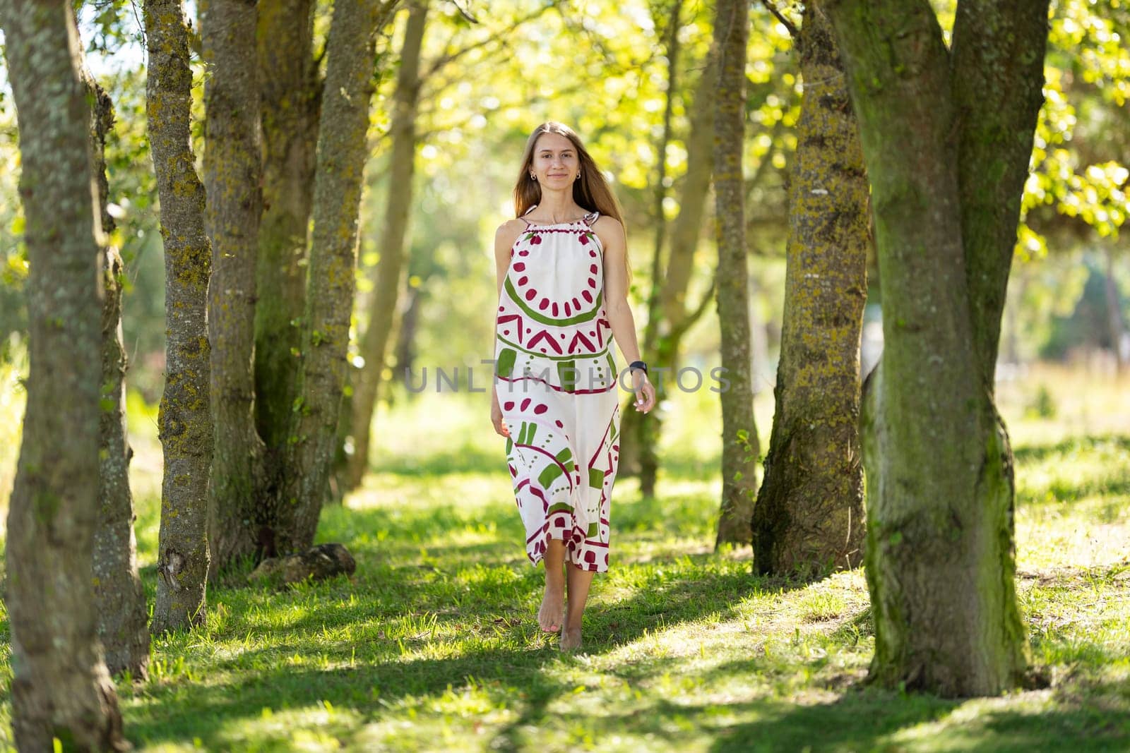 Young woman is enjoying a sunny day as she walks barefoot among trees