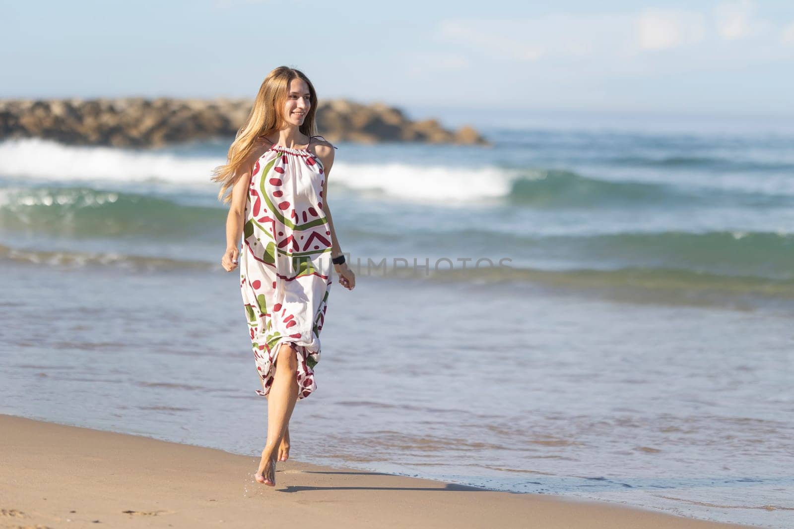 Young woman is running barefoot along the seashore, enjoying a sunny and carefree summer day