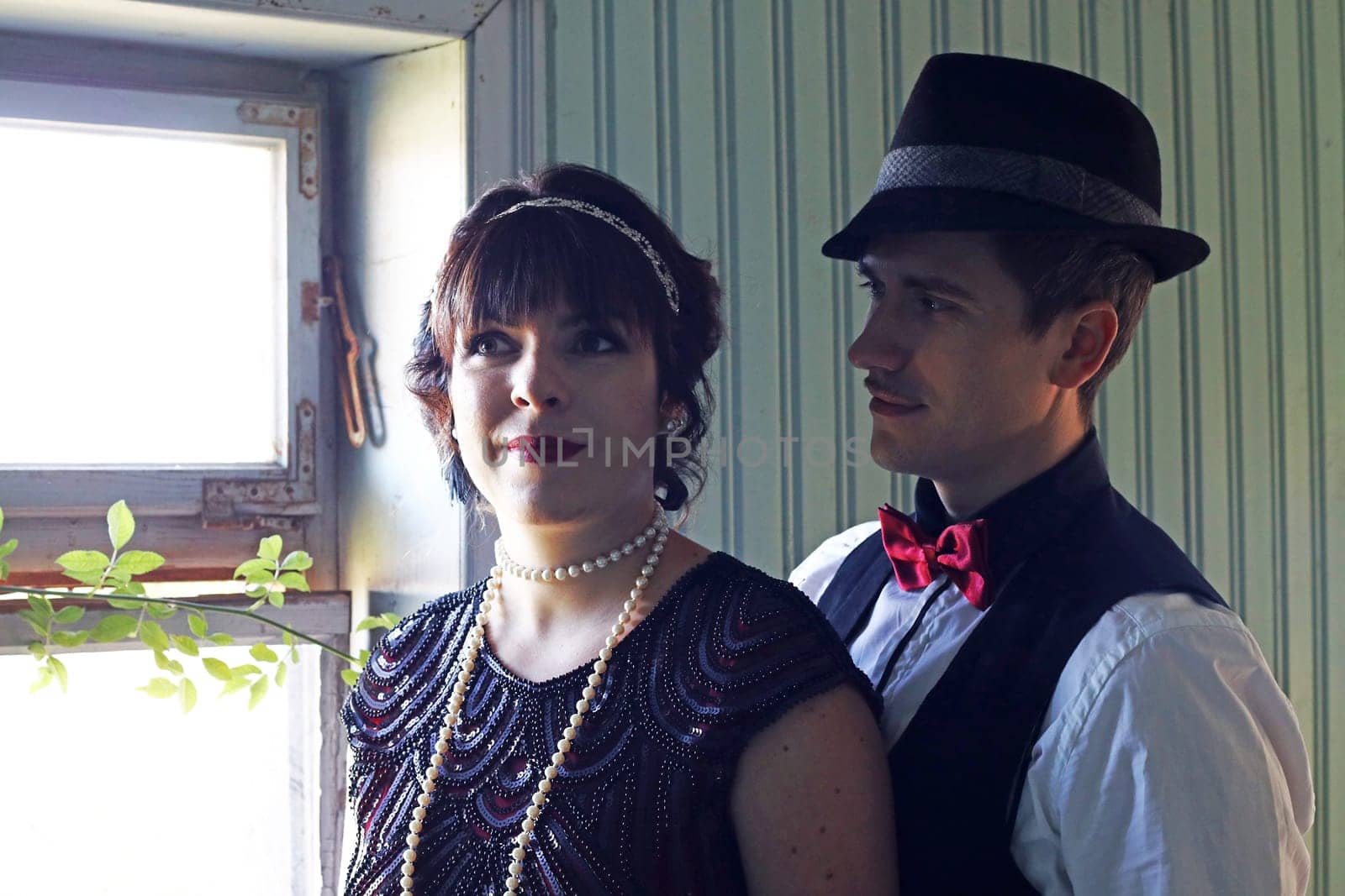 A pair of lovers in 20s retro style in light and shadow in front of a window