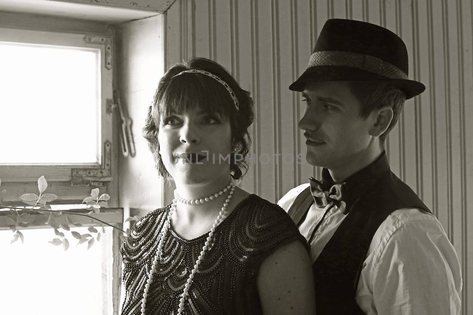 A pair of lovers in 20s retro style in light and shadow in front of a window