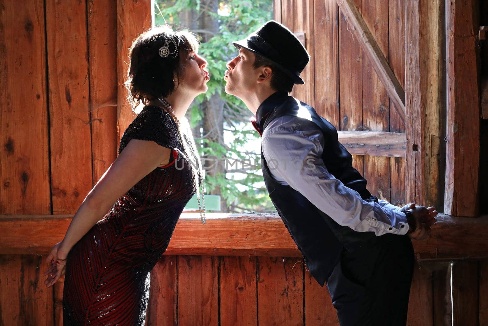 A pair of lovers in 20s retro style kissing in front of a window