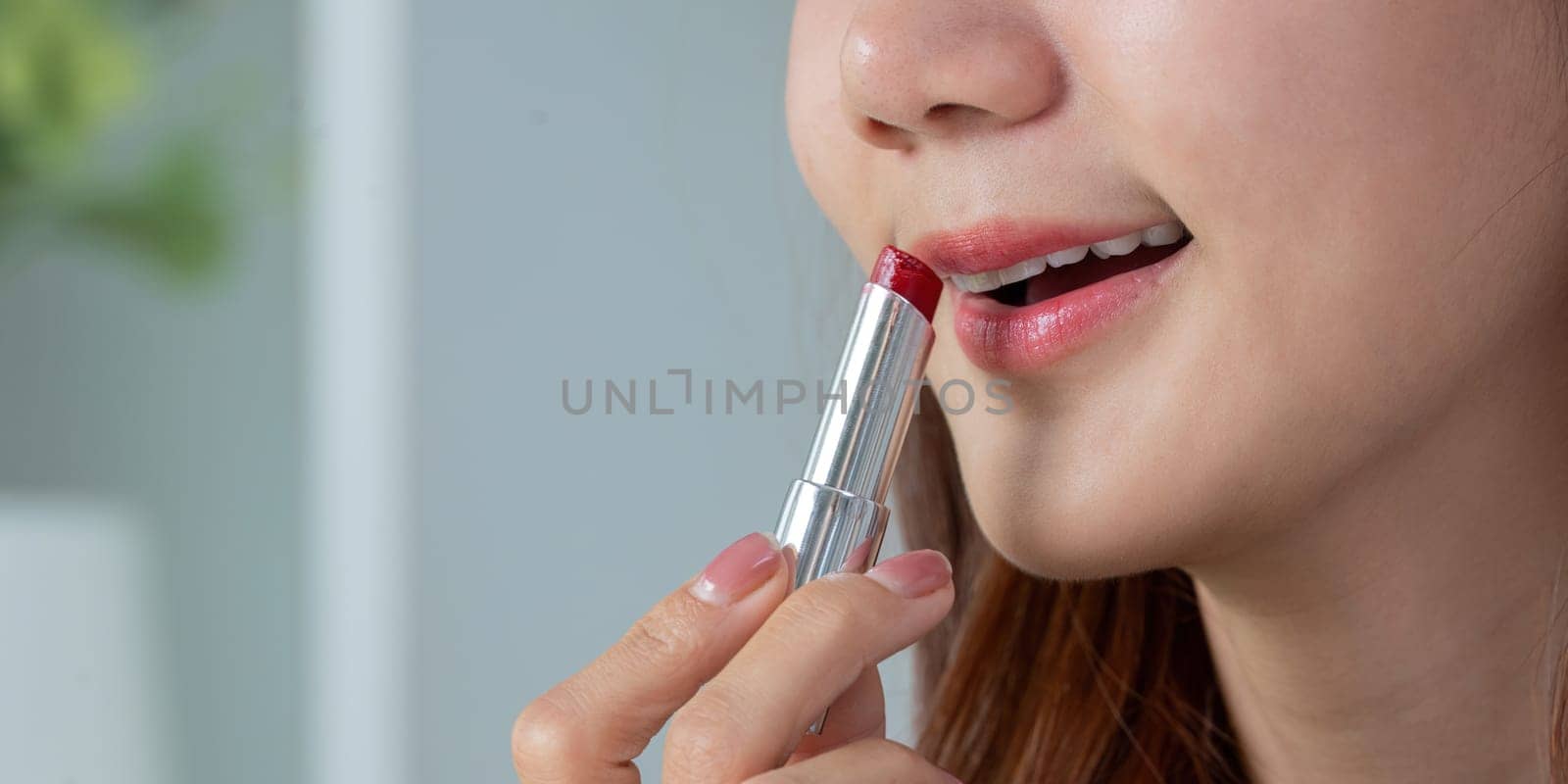 A woman applies vibrant red lipstick, showcasing her beauty routine and the art of makeup application with confidence.