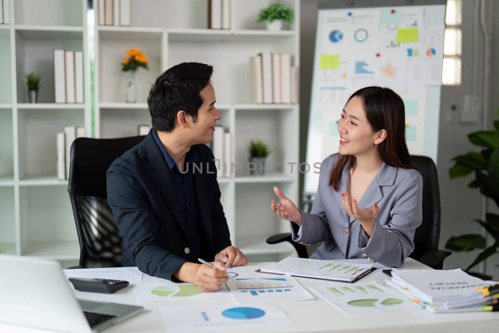 In a vibrant office setting, two colleagues are engaged in an animated conversation, exchanging insights and promoting teamwork.