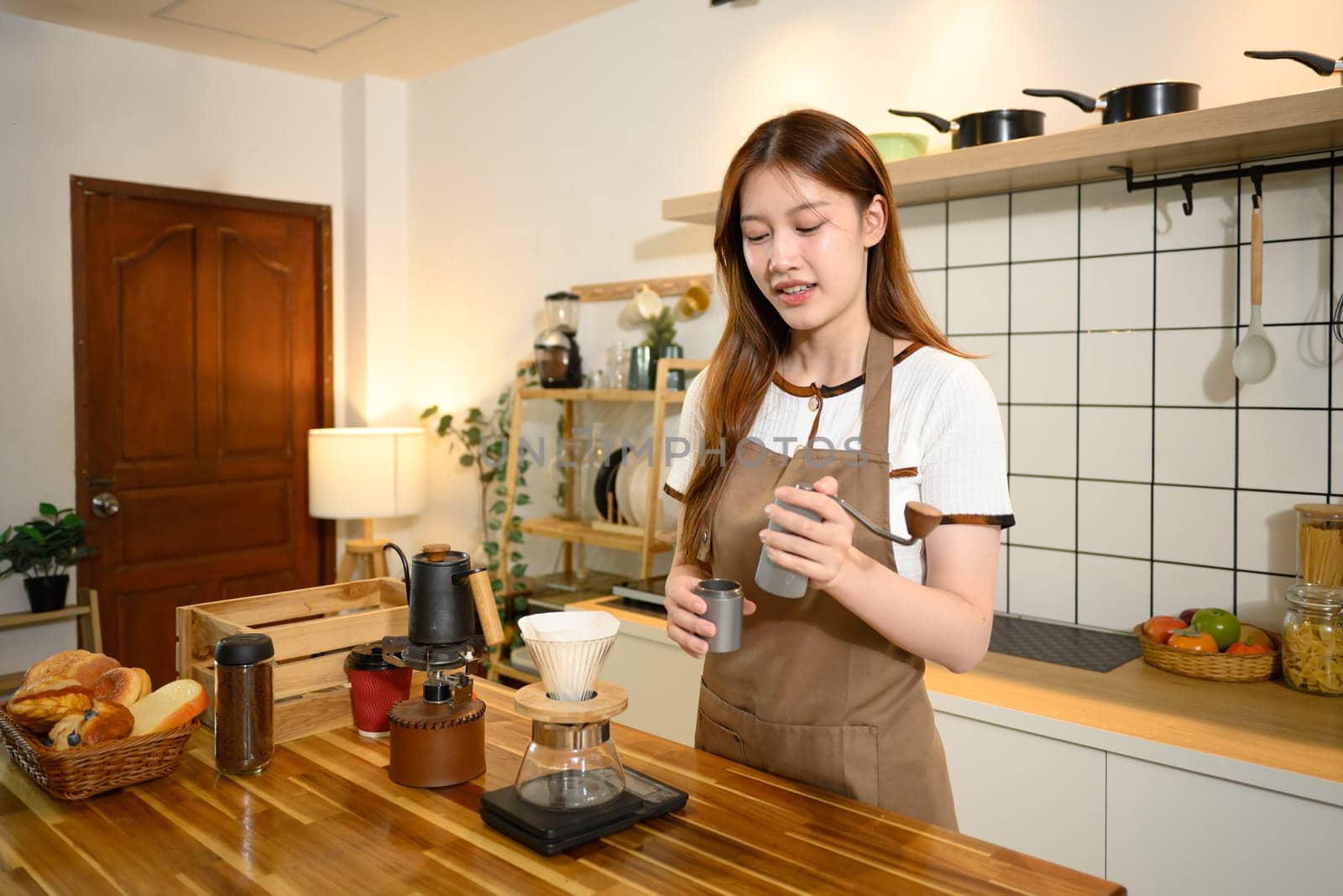 Young woman in apron preparing pour over coffee in a cozy home kitchen.