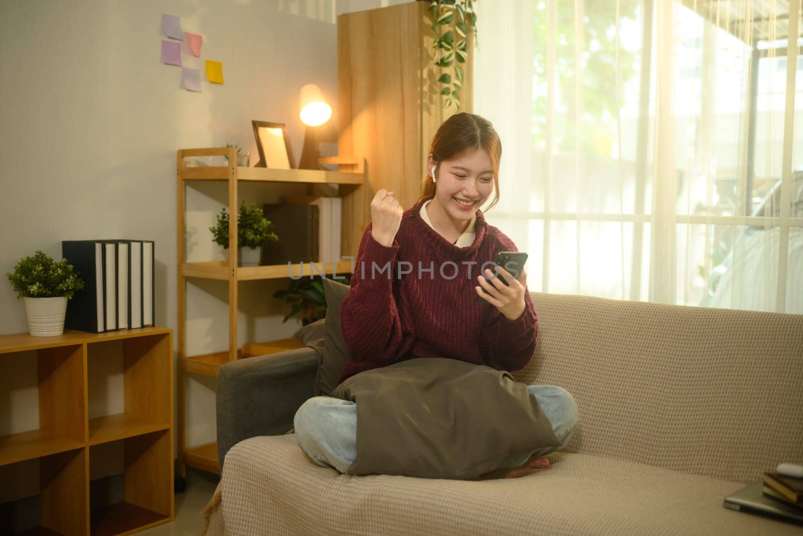 Cheerful young woman celebrating good news while looking at her smartphone.
